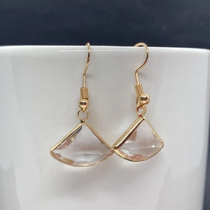 Detail of fan-shaped crystal earrings hanging on a white cup with gold metal frames