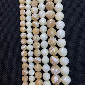 Natürliche runde Muschelperlen in Creme und Gold für DIY-Schmuck auf schwarzem Hintergrund