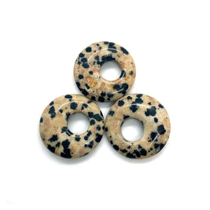 Macro view of three Dalmatian stone donut pendants with black spots on white background