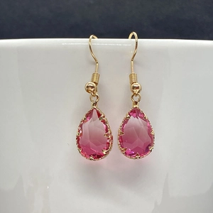 Detail of pink teardrop crystal earrings with gold claws and French hooks on a white vase