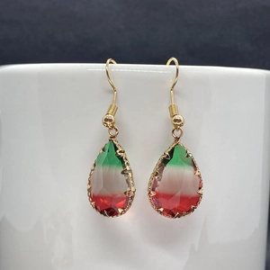 Detail of pear-shaped crystal earrings with green white red gradient on white ceramic cup