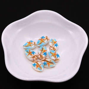 Detailed view of hand-painted turtle-shaped shell beads in a white ceramic dish