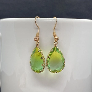 Detail of faceted teardrop crystal earrings in gradient green on a white ceramic mug edge