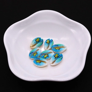 Detail of seven hand-painted turtle cowrie shells for DIY necklaces in a white ceramic dish