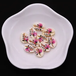 Macro detail of natural seashell charms with floral prints and LOVE text on a white tray