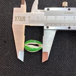 Close-up measurement of green and white conch shell bead with digital caliper