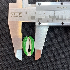 Macro view of a 1.5cm natural conch shell bead with vibrant green painted edges and calipers