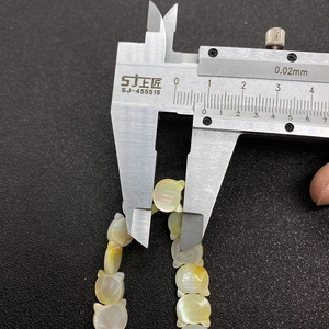 Macro shot measuring 9mm natural cat-shaped mother of pearl shell beads with a caliper
