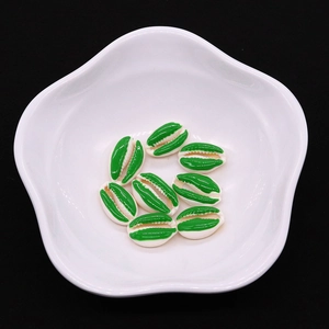 Macro detail of cowrie shell beads with green enamel finish in a white ceramic dish