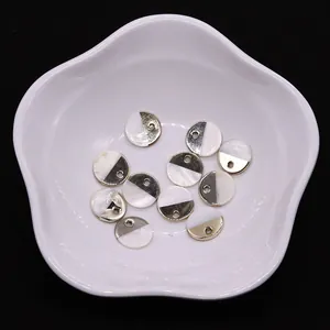 Détail de breloques rondes en nacre et métal doré pour bijoux DIY dans un plat blanc