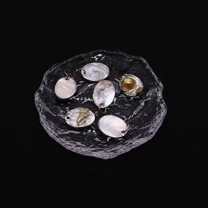 Vista macro di 6 ciondoli ovali in madreperla con bordi argentati e dettagli dorati