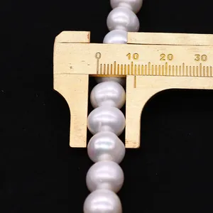 Messung einer 10mm weißen Süßwasserperle mit einem Messschieber aus Messing auf schwarzem Grund