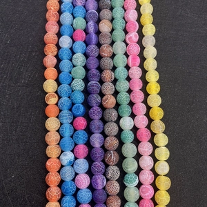 Macro shot of colorful weathered dragon vein agate round beads on a textured black background
