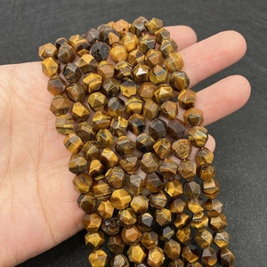 Nahaufnahme facettierter Tigerauge-Naturperlen mit goldener Textur in der Hand