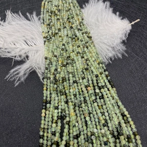 Macro shot of natural pale green faceted gemstone beads on dark textured background with feathers