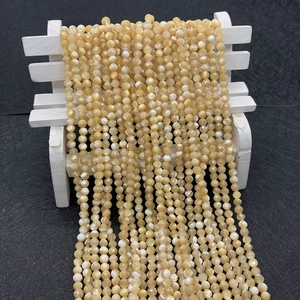 Close-up of faceted pale yellow natural shell beads 3-4mm hanging on a wooden stand
