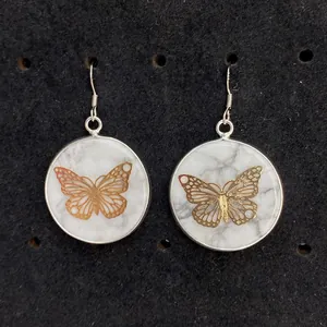 Nahaufnahme von weißen Marmor-Ohrringen mit goldenem Schmetterling und Silberhaken
