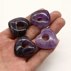 Detailansicht von vier herzförmigen lila Amethyst-Anhängern auf einem Handflächenhintergrund