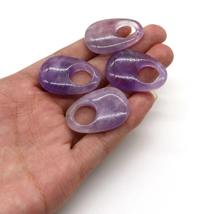 Close-up of four natural polished purple amethyst oval pendants held in a person's hand