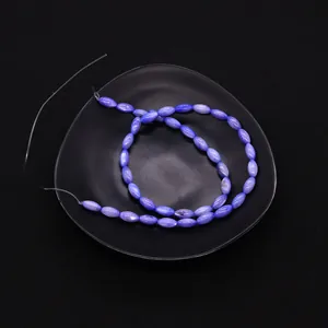 Primer plano de cuentas de concha azul-púrpura con forma de arroz en bandeja negra