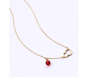 Macro detail of gold-plated hollow gourd pendant with a red agate bead on a delicate chain
