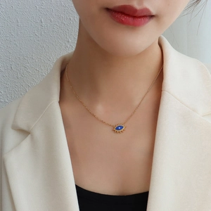 Goldene Evil Eye Kette mit blauem Anhänger an Model mit weißem Blazer getragen