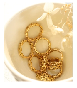 Stack of gold-plated geometric link rings displayed in a white ceramic bowl
