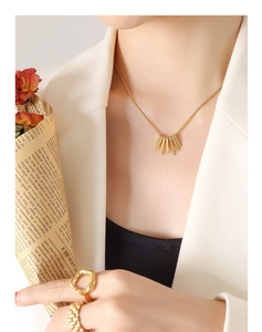 Close-up of a gold geometric square pendant necklace and rings worn with a stylish blazer