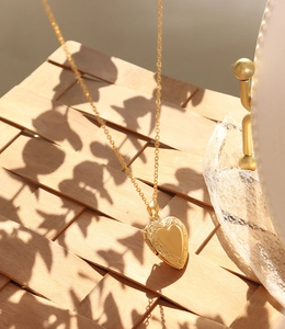 Détail d'un médaillon coeur doré à l'or 18K avec gravures florales sur support en bois