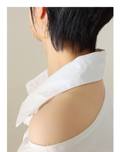 Close-up of a large gold star-shaped hoop earring worn by a model in a minimalist style