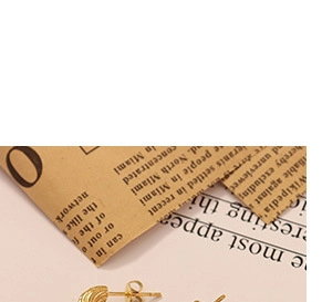 Detaillierte Nahaufnahme goldener Flügelohrringe mit feiner Textur auf Vintage-Zeitungsuntergrund