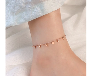 Détail de la chevillère en or rose avec des breloques disques polis sur fond de tissu doux