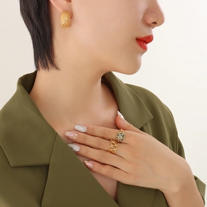 Goldene Gitter-Ohrringe und strukturierte Ringe getragen von Model in olivfarbenem Blazer