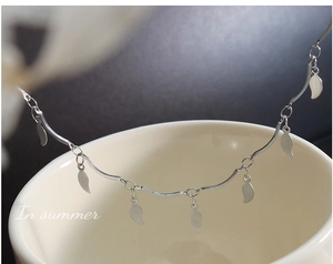 Detalle del collar minimalista de plata con borlas de hojas sobre una taza blanca