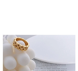 Primer plano de un anillo dorado con textura de engranaje sobre un portavelas blanco liso