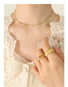 Detail einer eleganten Goldperlenkette und strukturierten Ringen auf weißem Spitzenkragen