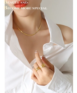 Golden snake chain necklace and geometric rings set worn on a white shirt background