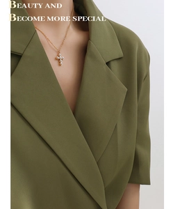 Détail du collier avec pendentif croix en perles porté sur un blazer vert élégant