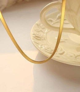 Macro detail of a 3mm flat 18K gold-plated snake chain with polished metallic texture