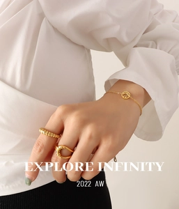 Detail von goldenem Armband mit Smiley-Anhänger und Croissant-Ring an einem weiblichen Model