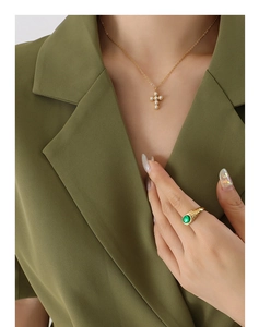 Gros plan du collier pendentif croix en perles et bague gemme verte sur mannequin