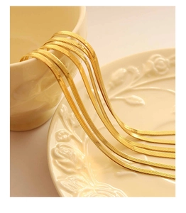 Close-up of golden flat herringbone snake chain draped over elegant white ceramic