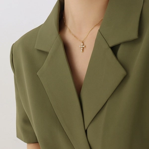 Collier à pendentif croix en or avec perles sur mannequin en veste verte chic