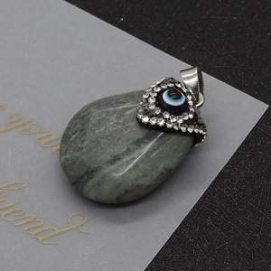 Macro detail of teardrop evil eye pendant with crystal inlay on a natural stone base