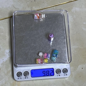Dettaglio ravvicinato di 5 ciondoli a forma di mini bottiglia colorata su bilancia