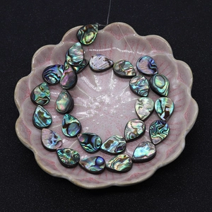 Macro shot of iridescent teardrop abalone shell beads on a pink porcelain plate