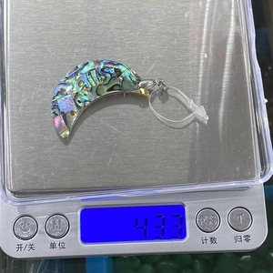 Détail d'un pendentif lune en nacre d'abalone sur une balance pesant environ 4,33g