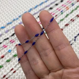 Detail of silver chain with dark blue enamel oval beads held over colorful variations
