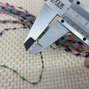 Macro detail of silver bead chain with green olive beads measured by a caliper tool