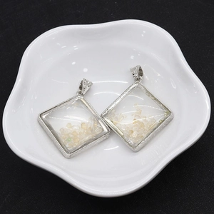 Close-up of diamond-shaped silver pendants filled with champagne crystal stone on white plate